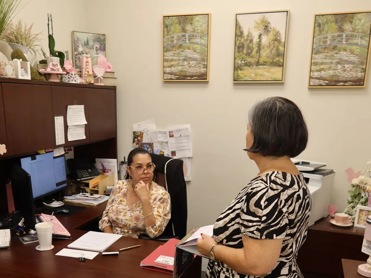 Una integrante del personal en su escritorio conversando con una mujer en la oficina del bufete en Miami