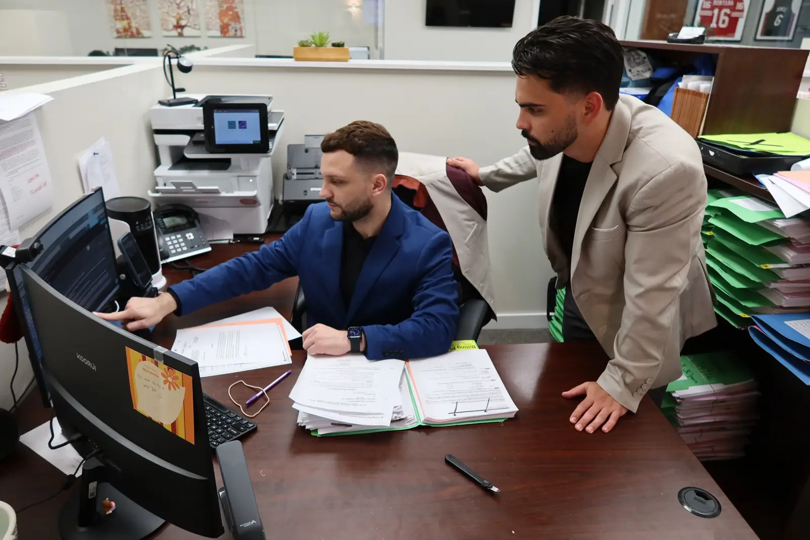 Dos miembros del personal del bufete revisando el expediente de un cliente en una computadora en la oficina de Miami